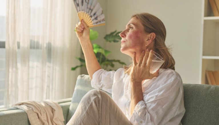 Woman in her late 40s touching her face during a menopause hot flash β does exercise help with hot flashes